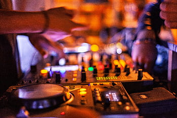Close-up of DJ mixing console with hands adjusting controls at a lively nightclub. HD wallpaper