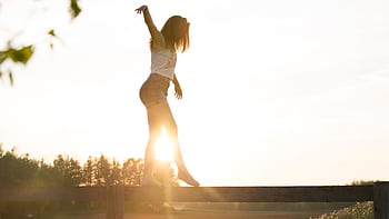 A young woman balancing on a fence during a serene sunrise, exuding dom and joy. HD wallpaper