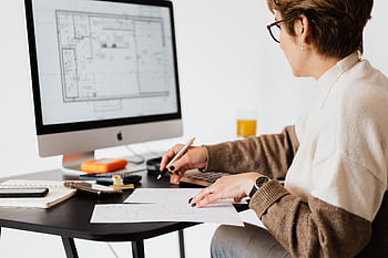 Woman designing architectural blueprints using computer in a modern office setting. HD wallpaper