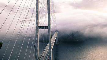 A dramatic view of a fog-covered suspension bridge with cables and the ocean below. HD wallpaper