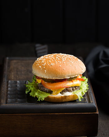 Close-up of a delicious cheeseburger with lettuce, tomato, and cheese on a sesame seed bun. HD phone wallpaper