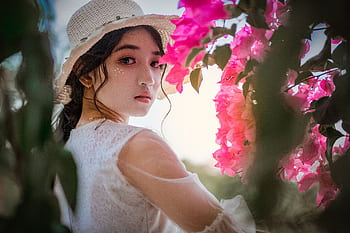 Elegant portrait of a woman in a white dress and hat, surrounded by vibrant pink bougainvillea flowers. HD wallpaper