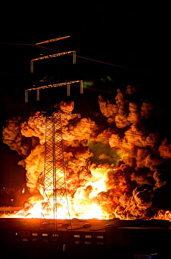 A powerful nighttime explosion at a factory with flames and smoke under power lines. HD phone wallpaper
