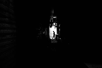 Black and white capturing a silhouette of a man walking in a dimly lit alley. HD wallpaper