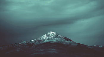 A dramatic snow-capped mountain peak in Algeria set against a moody sky, perfect for winter landscapes. HD wallpaper
