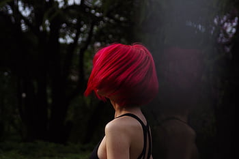Woman with vibrant red hair turns away in a shadowy forest, striking dynamic pose in natural setting. HD wallpaper