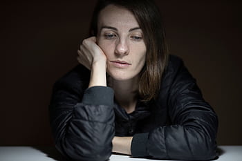 A woman in thought with a serious expression, indoors, in a low-light setting. HD wallpaper