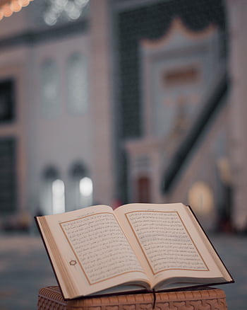 A beautifully open Quran resting on a stand within the serene environment of a mosque interior. HD phone wallpaper