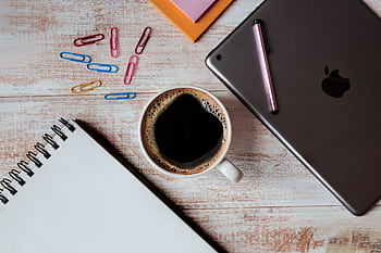 Top view of a creative workspace featuring a tablet, coffee, notebook, and paperclips on a wooden desk. HD wallpaper
