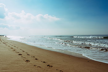 Tranquil ocean shore with footprints in the sand under a clear blue sky. HD wallpaper