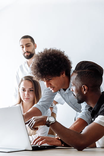Group of professionals engaging in a collaborative discussion around a laptop in a modern office setting. HD phone wallpaper