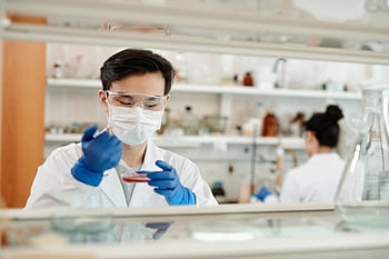 Researcher in a lab coat working on a scientific experiment with a petri dish and protective gear. HD wallpaper