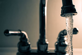 A detailed shot of water flowing from a steel faucet, ideal for themes on cleanliness or plumbing. HD wallpaper