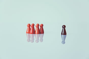 Red game pieces grouped with one isolated piece symbolizing social distancing on a reflective surface. HD wallpaper