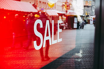 Red sale sign on storefront window reflecting a busy urban street scene, capturing city life. HD wallpaper