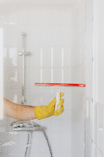 A person wearing a yellow glove cleans a shower glass with a squeegee, emphasizing hygiene and cleanliness. HD phone wallpaper