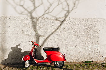 A vibrant red vintage scooter parked against a textured wall in Porto, Portugal. HD wallpaper