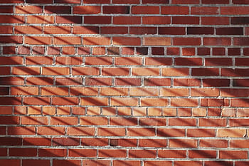 Red brick wall with striking shadows creating a textured pattern. HD wallpaper