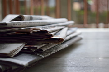 A close-up of a stack of newspapers resting on a desk, symbolizing information and media. HD wallpaper