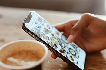 Hand browsing social media on a smart next to a cup of coffee indoors. HD wallpaper