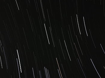 Long exposure of star trails creating a dynamic pattern in the night sky. HD wallpaper