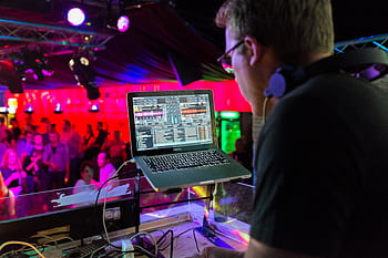A DJ plays music using a laptop in a lively nightclub with a vibrant crowd and colorful lighting. HD wallpaper