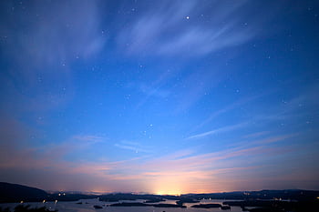 A serene skyscape featuring stars, a glowing horizon, and streaking clouds at twilight. HD wallpaper