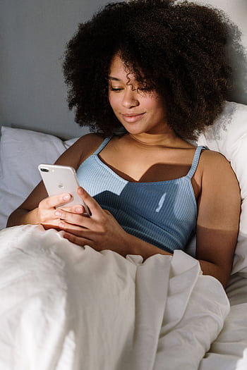 African American woman enjoying a cozy morning in bed, using a smart. HD phone wallpaper