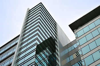 Low angle view of a modern skyscraper with glass facade reflecting the sky. HD wallpaper