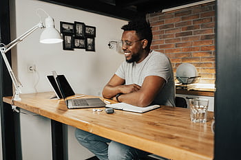 African American man smiling and working remotely from home using a laptop and digital tablet. HD wallpaper