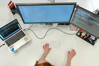 A female software engineer coding on dual monitors and a laptop in an office setting. HD wallpaper