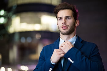Portrait of a stylish businessman adjusting his suit in an urban night setting. HD wallpaper