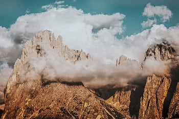 Breathtaking view of Dolomites peaks enveloped by clouds under a blue sky. Perfect for nature enthusiasts. HD wallpaper