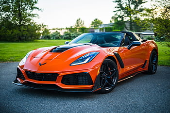 A sleek orange convertible sports car elegantly parked on a scenic outdoor road. HD wallpaper