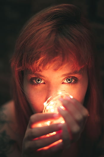 Artistic portrait of a red-haired woman holding fairy lights, creating a warm and moody atmosphere. HD phone wallpaper