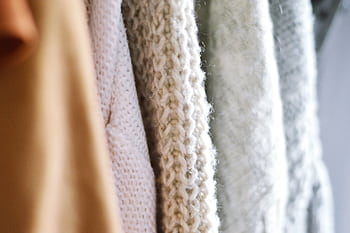 Detailed view of multiple woolen knitted sweaters in soft, neutral colors emphasizing texture and warmth. HD wallpaper
