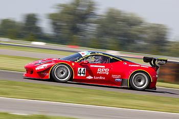 High-speed red race car in motion on track, captured in vibrant daylight. HD wallpaper