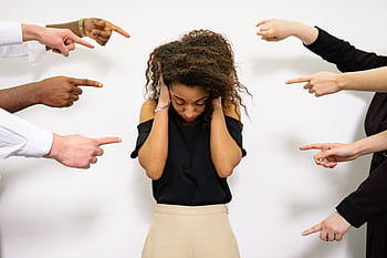 A young woman with curly hair looks distressed as multiple hands point accusatory fingers at her. HD wallpaper