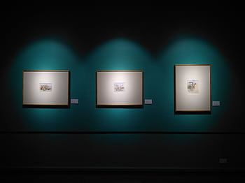 Framed artworks illuminated on a museum wall in Manila, capturing modern aesthetics. HD wallpaper