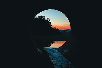 A tranquil view through a tunnel at sunset, capturing reflections on a calm body of water. HD wallpaper