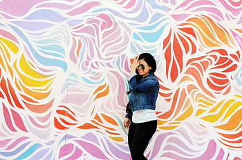 A woman in a denim jacket poses joyfully against a vibrant mural in Asbury Park, NJ. HD wallpaper
