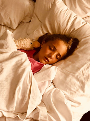 Young girl sleeping peacefully with stuffed animal in a cozy white bed. HD phone wallpaper