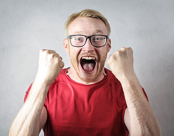 A cheerful man in a red shirt expressing excitement indoors. HD wallpaper