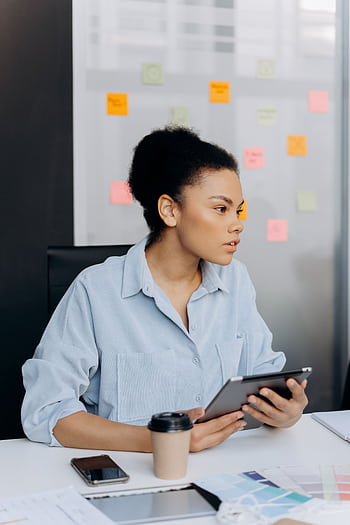 Professional female analyzing work on a tablet in a modern office environment. HD phone wallpaper
