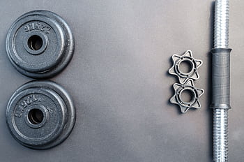 Barbell and two dumbbell weights arranged on a neutral gray surface. HD wallpaper