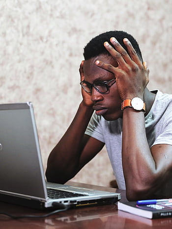 A man appears frustrated while working on a laptop in an office setting, showcasing remote work challenges. HD phone wallpaper
