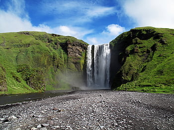 A breathtaking view of a waterfall cascading amidst vibrant green hills under a blue sky. HD wallpaper