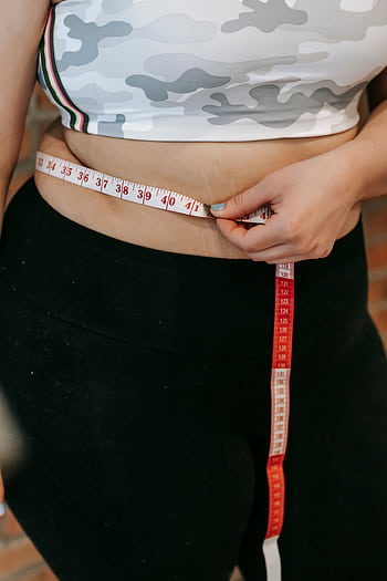 A woman measures her waist using a red measuring tape while wearing activewear. HD phone wallpaper