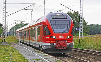 A vibrant red electric train arrives at a rural railway station, showcasing modern public transport. HD wallpaper