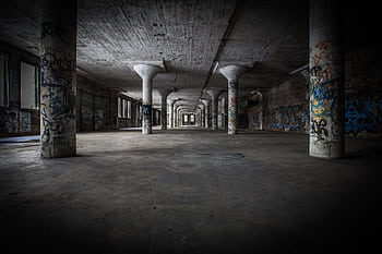 Moody interior of an abandoned warehouse featuring graffiti-covered columns and empty space. HD wallpaper